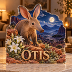 Front view of personalized aardvark desert lily moon valley acrylic plaque with sample name OTIS, displayed in a softly blurred warm naturalist sitting room at dusk on pale stone console