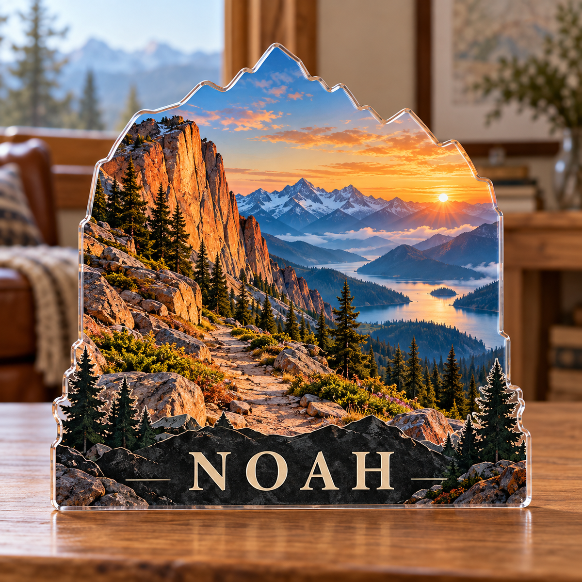 Front view of a personalized alpine ridge sunrise trail custom-shape acrylic plaque with example name NOAH, displayed in a softly blurred mountain cabin with a landscape window