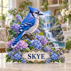 Front view of a blue jay hydrangea woodland custom-shape acrylic plaque with example name SKYE, displayed in a softly blurred botanical reading room on pale stone console